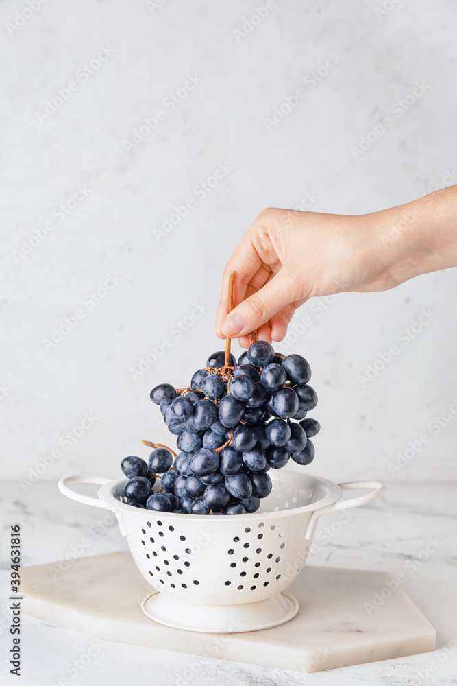 Female hand with fresh grapes and colander on light background