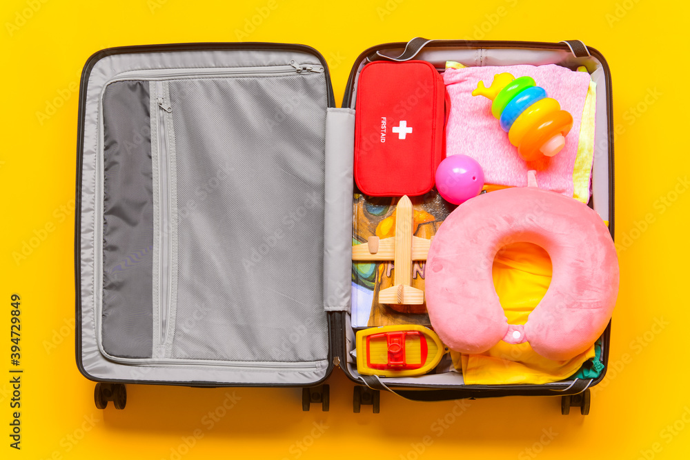 Composition with child accessories in suitcase on color background. Travel concept