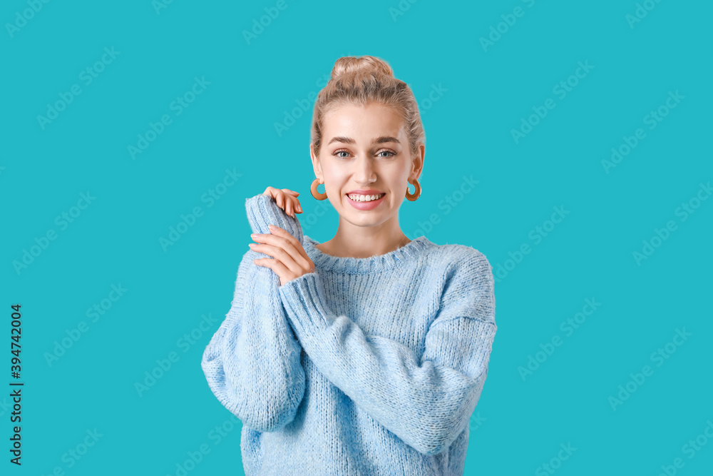 Beautiful young woman in warm sweater on color background