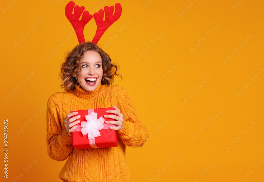 cheerful surprised   woman  with red deer antlers holds a Christmas gift and laughing a colored yell