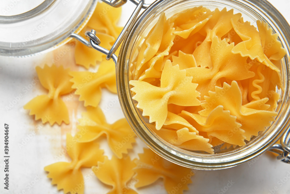 Glass jar with uncooked pasta on light background