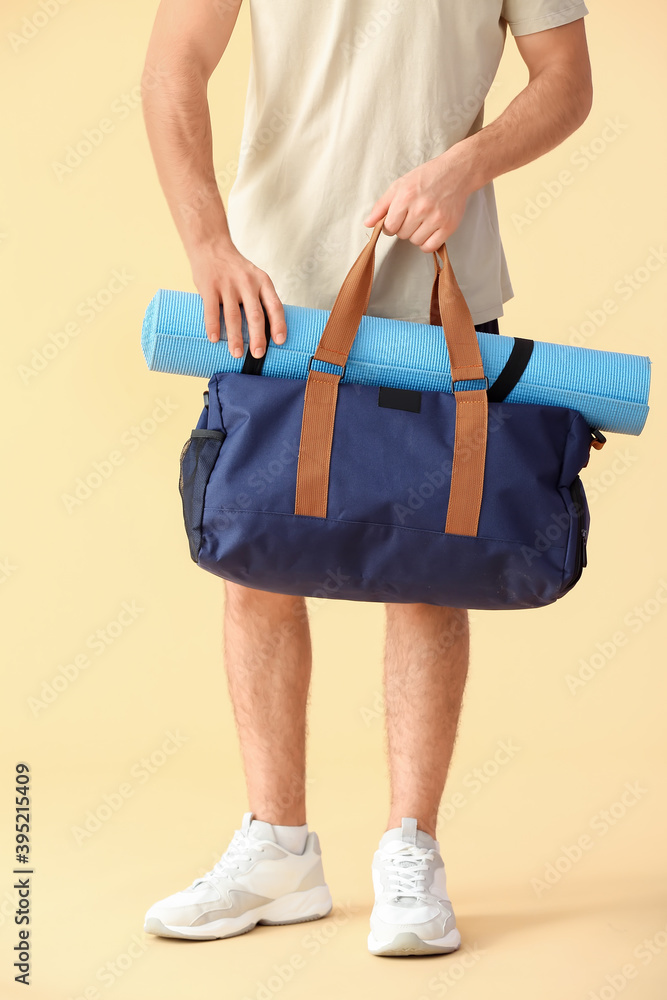 Sporty young man with bag and yoga mat on color background