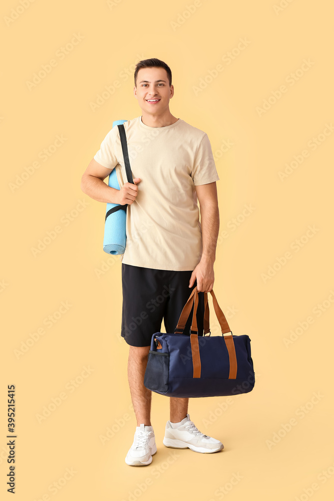 Sporty young man with bag and yoga mat on color background