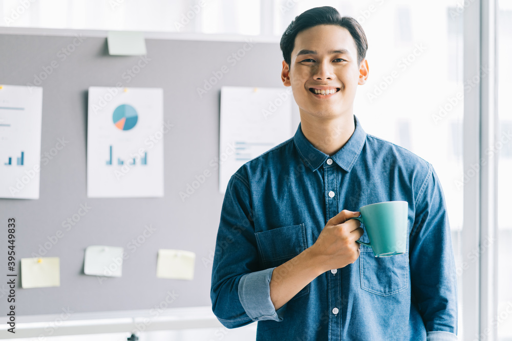 Asian man holding coffee cup standing smiling with planning board background