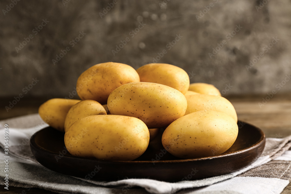 Plate with raw potatoes on wooden table