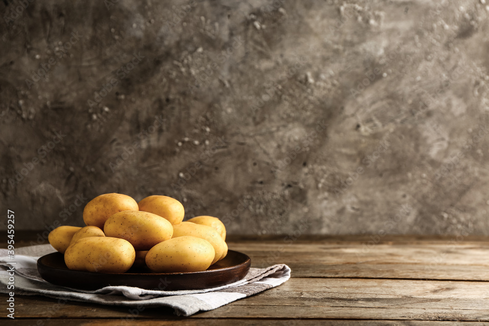 Plate with raw potatoes on wooden table