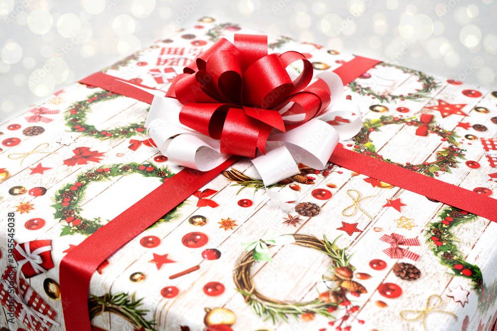 A Christmas gift wrapped in beautiful paper and a red and white bow on a white background. Christmas