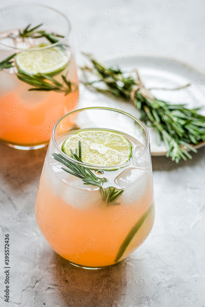 sliced lime, rosemary, plate and juice in glass on stone table background