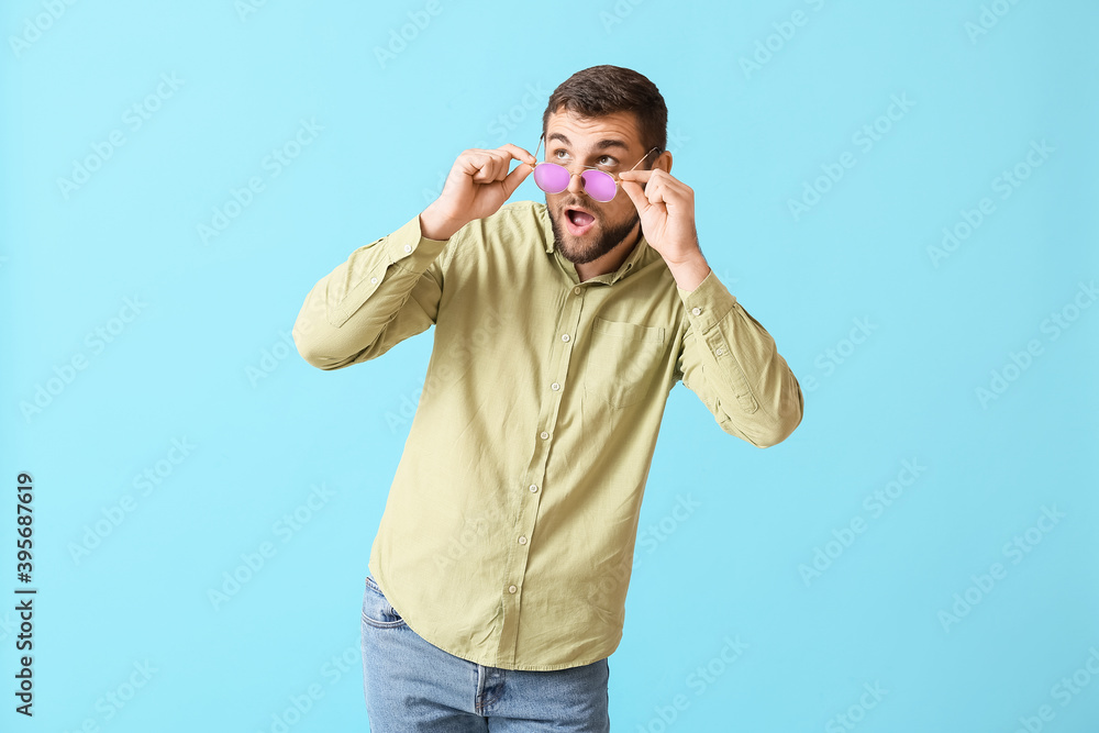 Surprised man with stylish sunglasses on color background