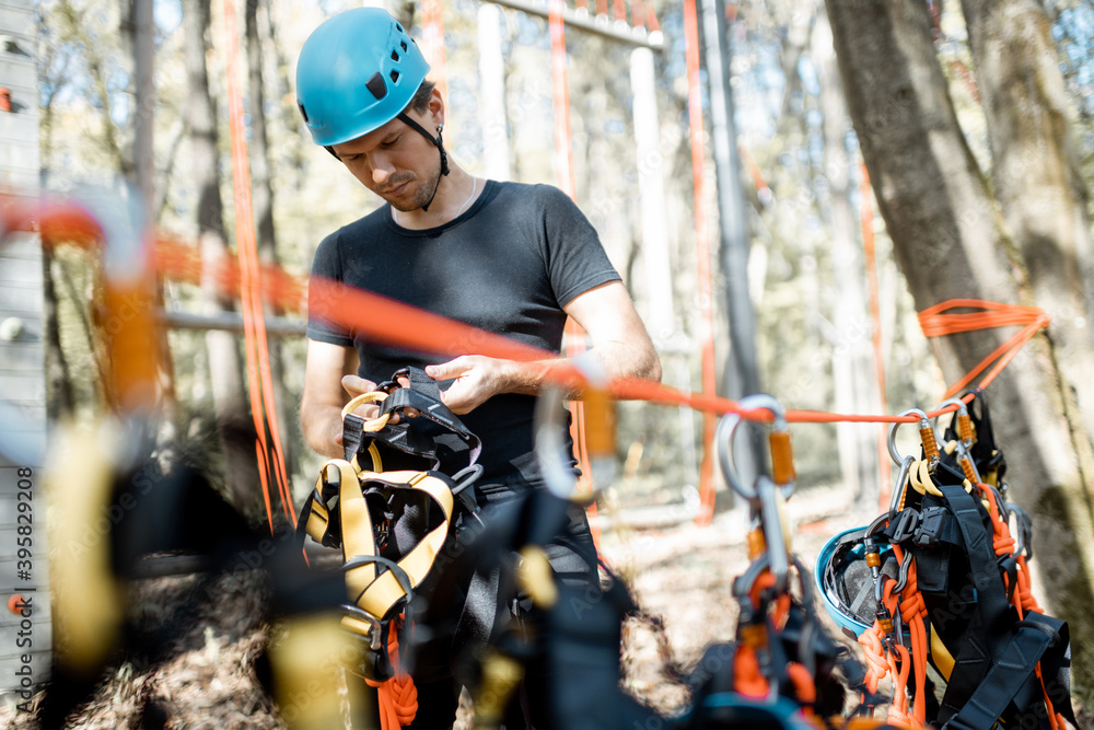 Handsome man wearing safety equipment for climbing at amusement park, preparing for climbing on the 