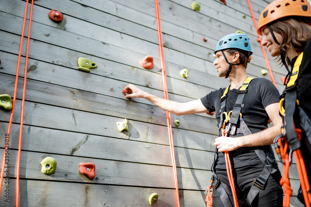 Male instructor with young woman near the climbing wall at amusement park outdoors, ready for climbi