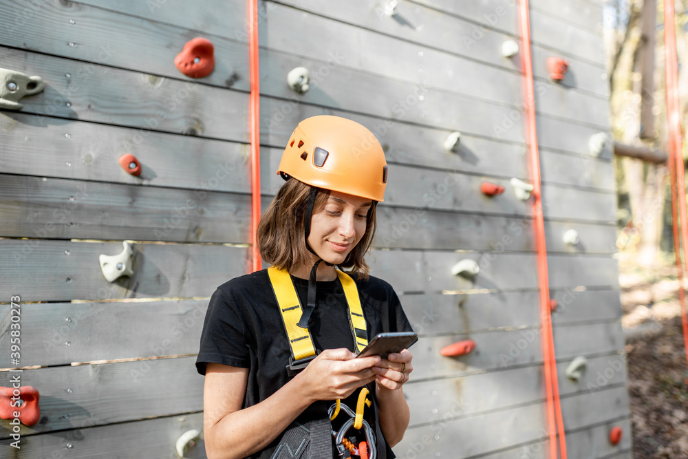 Young woman in protective sports equipment with a smart phone near the climbing wall outdoors