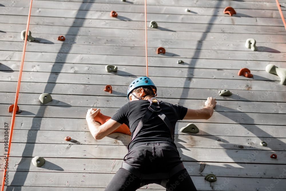 Well-equipped man climbing the wall outdoors in the park for sports entertainment