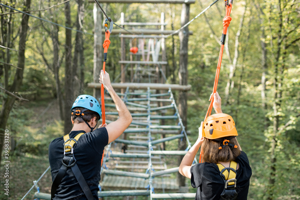 Well-equipped man and woman having an active recreation, climbing ropes in the park with obstacles o