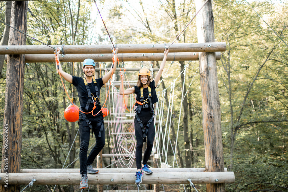 Well-equipped man and woman having an active recreation, climbing ropes in the park with obstacles o