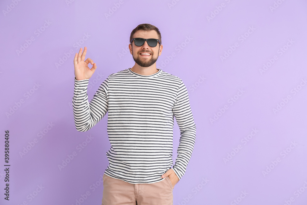 Handsome man with stylish sunglasses showing OK gesture on color background