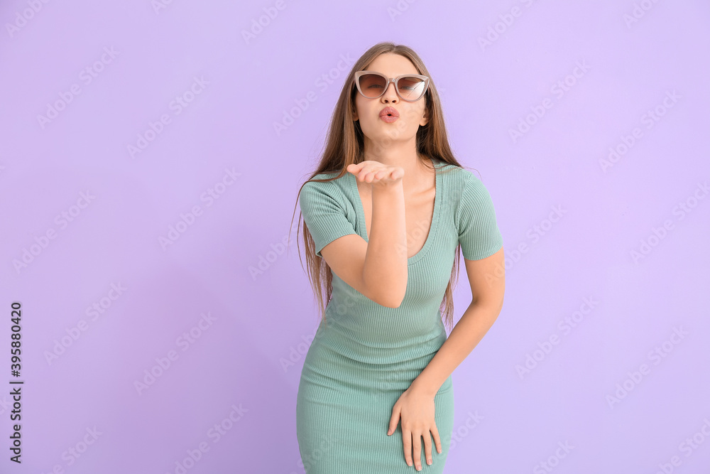 Beautiful woman with stylish sunglasses blowing kiss on color background