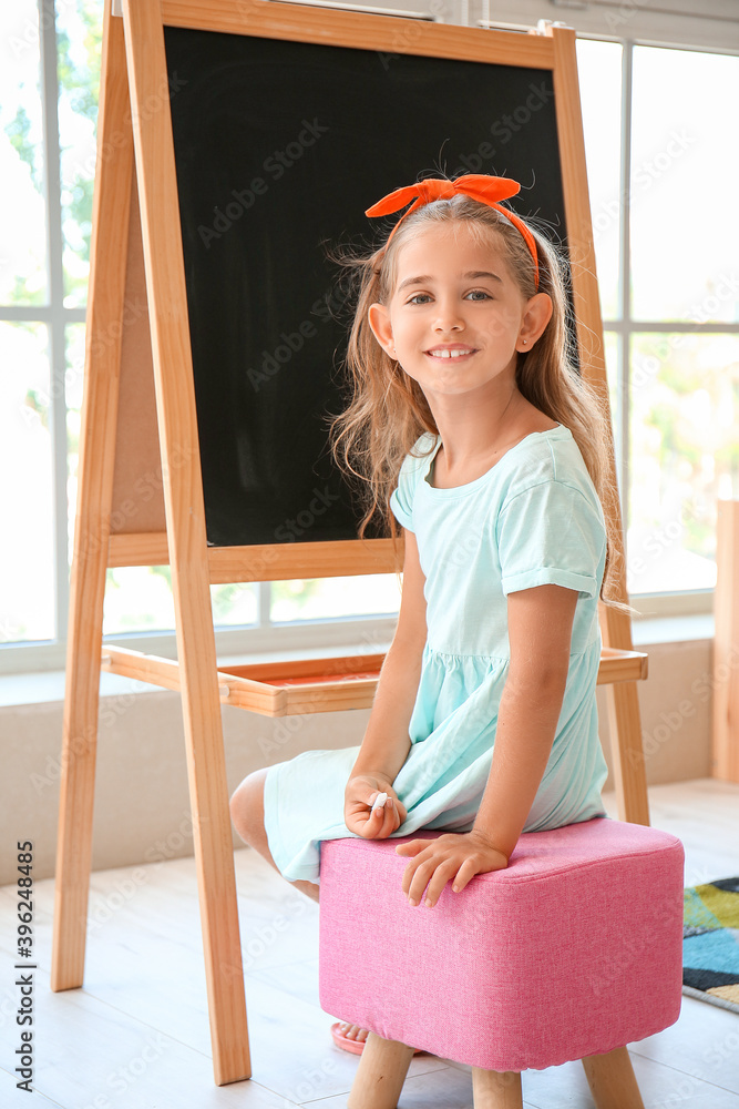 Happy little girl with chalk near blackboard in kindergarten