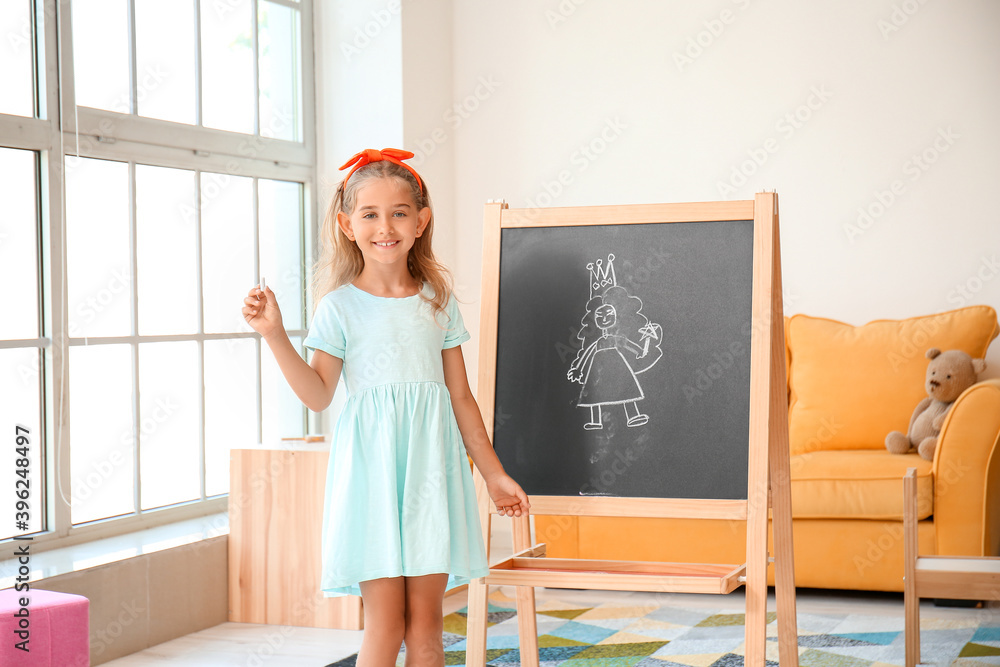 Cute little girl with drawn princess on blackboard in kindergarten