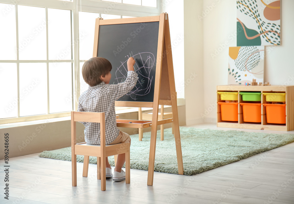 Cute little boy drawing on blackboard in kindergarten