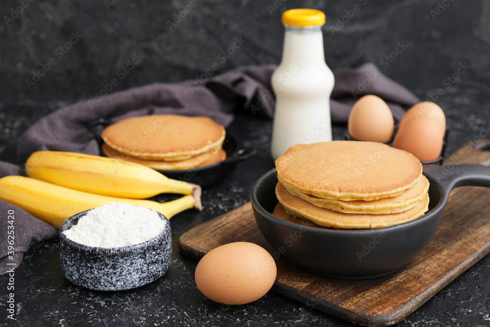 Tasty banana pancakes with ingredients on dark background