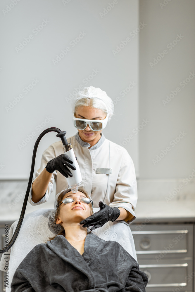 Professional doctor in protective wear making a laser rejuvenation treatment for a young woman clien