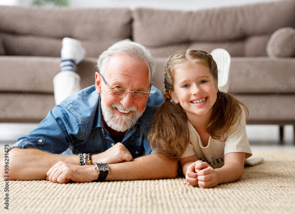 Cheerful kid girl with grandfather lying on the floor at home