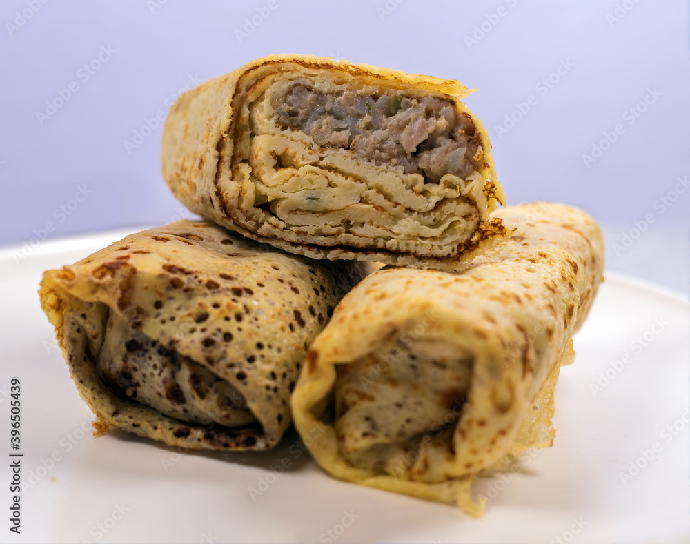 The homemdade pancakes filled by meat on the white plate on the marble countertop table.