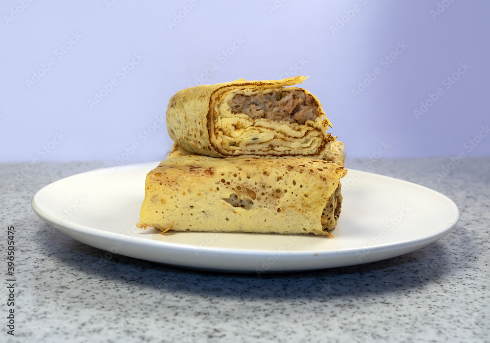 The homemdade pancakes filled by meat on the white plate on the marble countertop table.