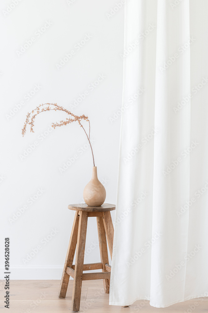 Dry Forsythia branch in a wooden vase on a stool by a white curtain