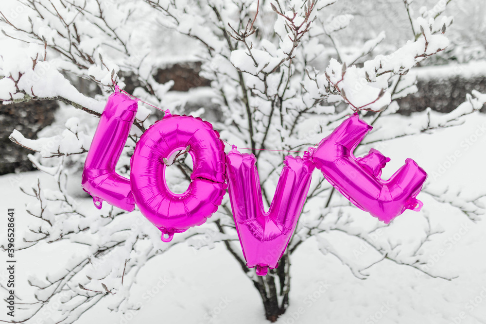 Pink love balloon word hanging on a snowy tree