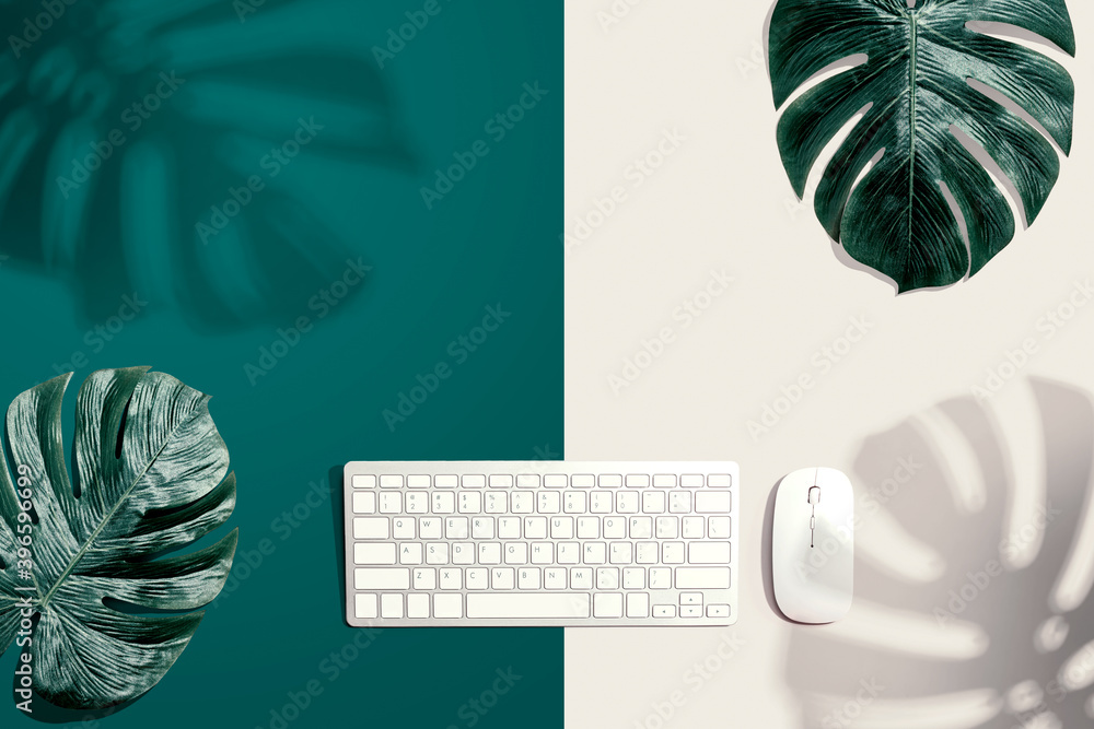 Computer keyboard with tropical leaves and shadow - flat lay