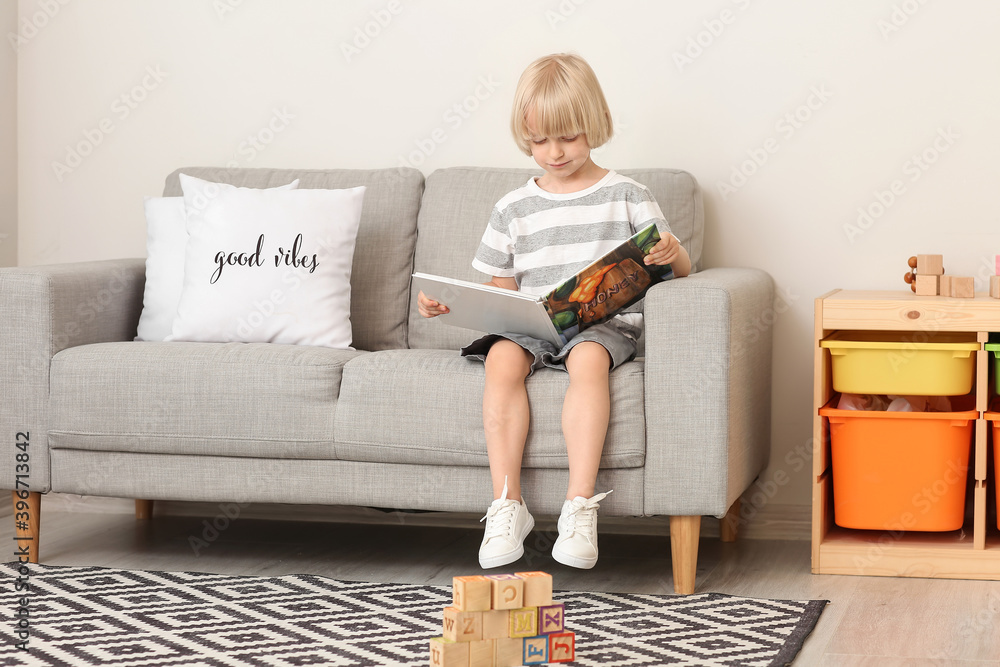 Cute little boy reading book on sofa at home