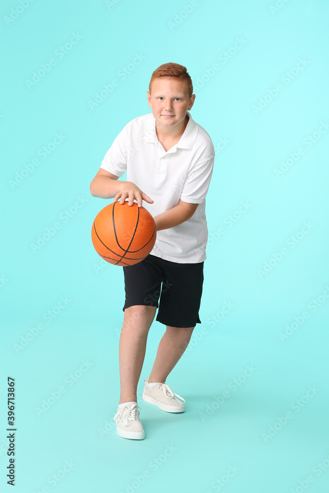 Sporty teenage boy playing basketball on color background