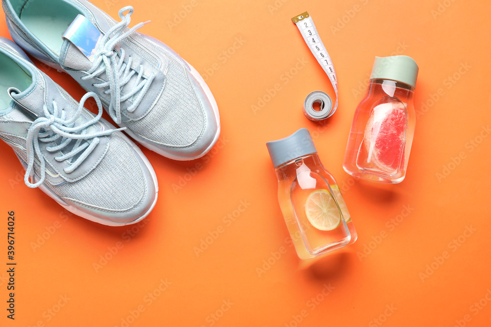 Bottles of infused water, sports shoes and measuring tape on color background