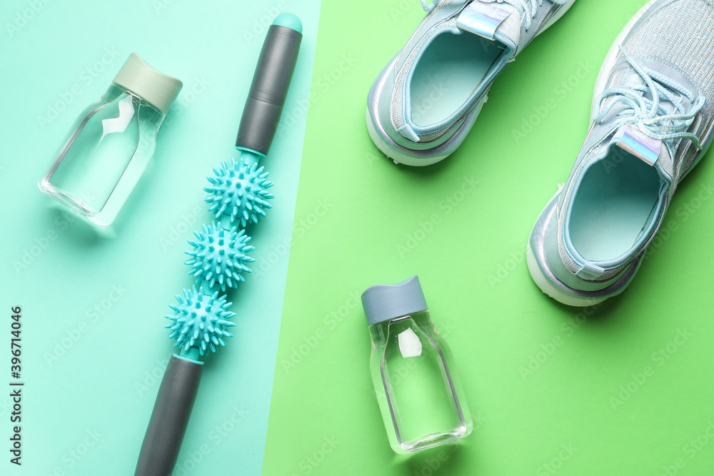 Bottles of water, sports shoes and body roller on color background