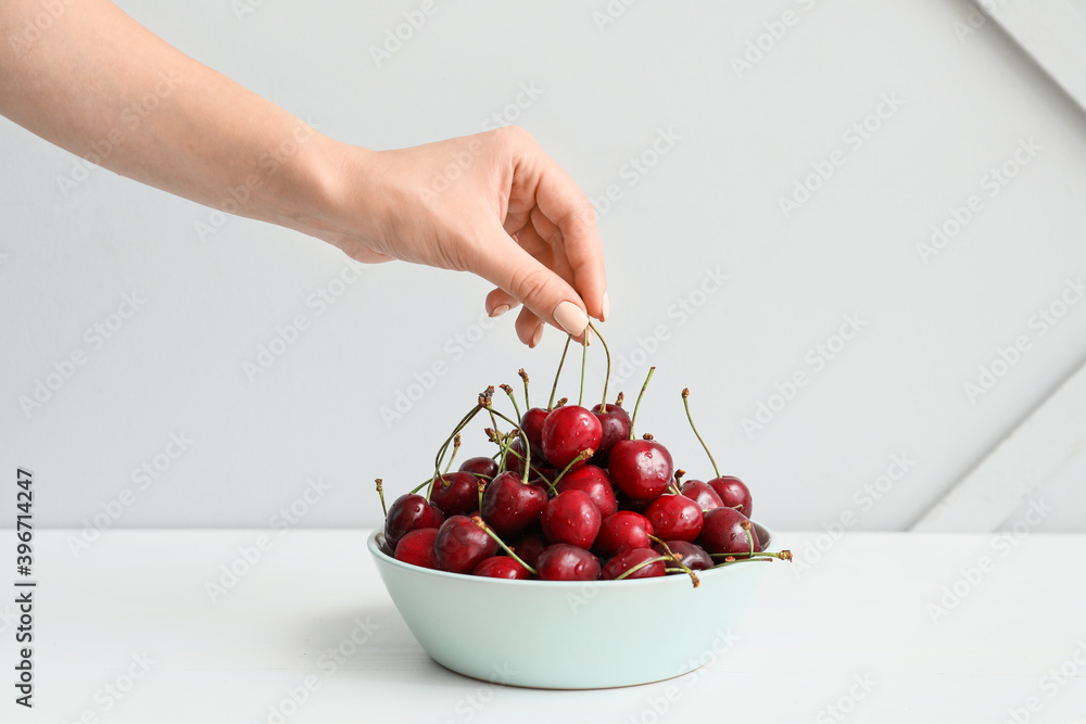 Female hand with bowl of tasty cherry on light background