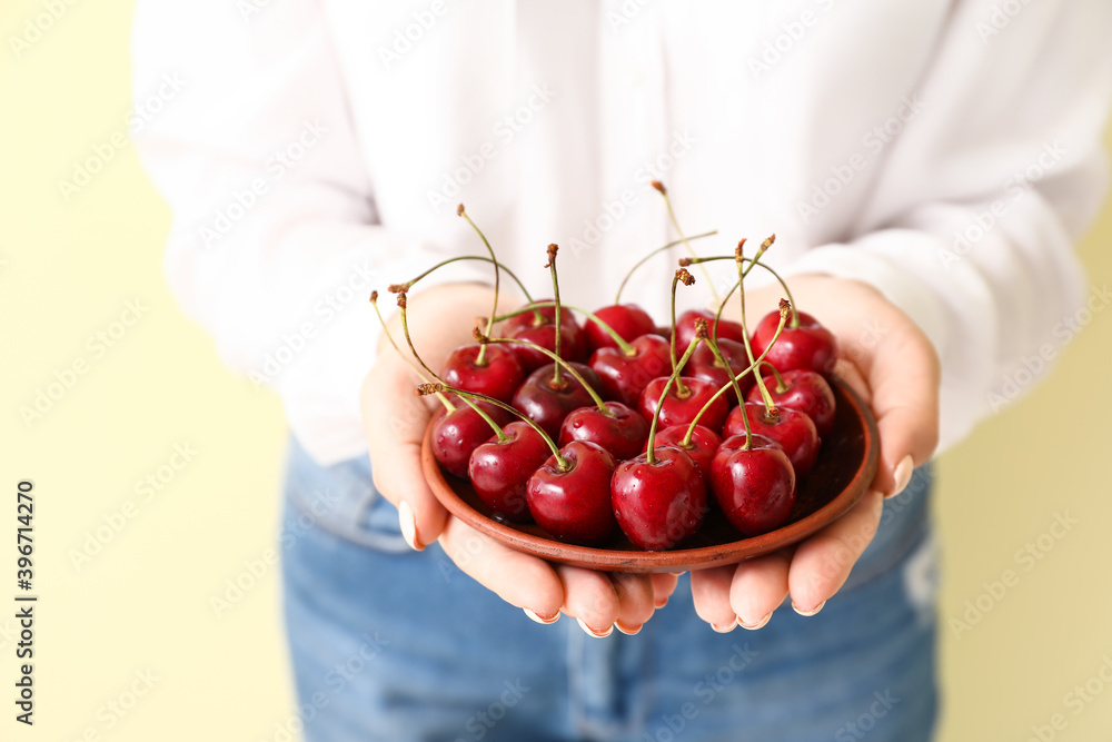 Woman with plate of tasty cherry on color background