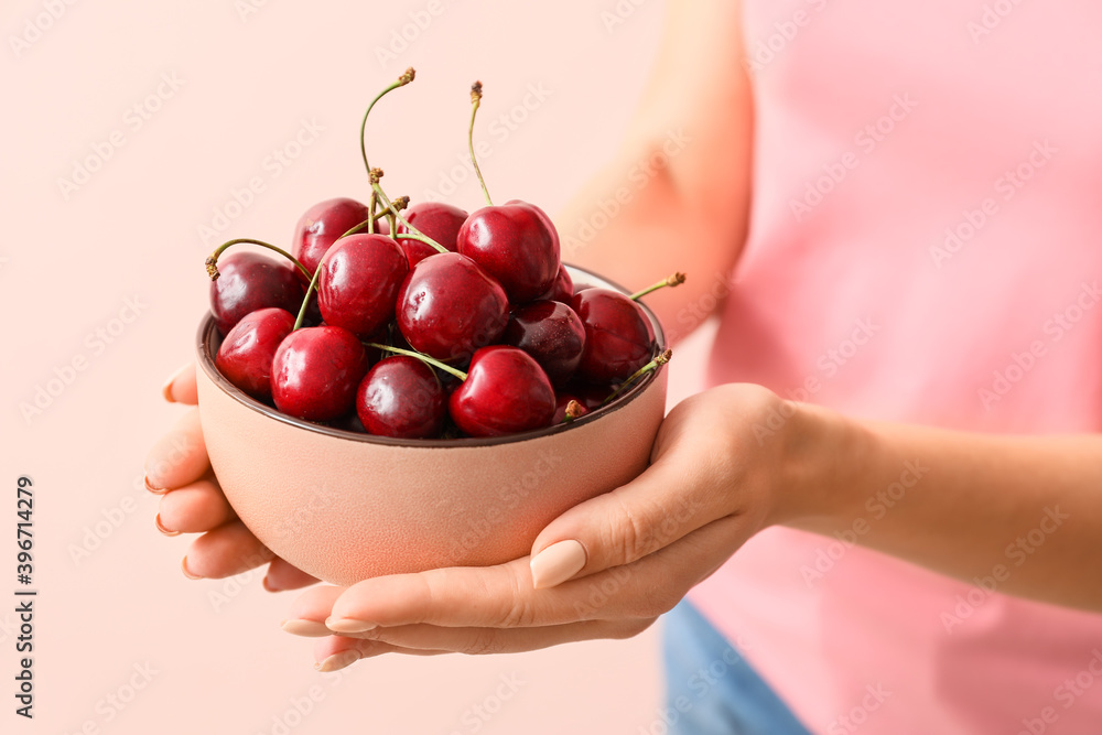 Woman with bowl of tasty cherry on color background