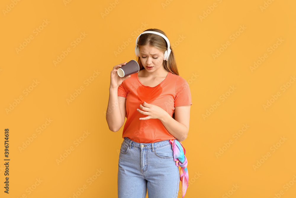 Young woman with coffee stains on her t-shirt and headphones on color background