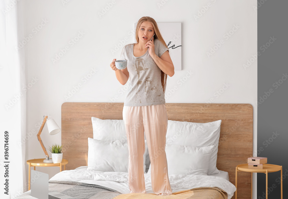 Young woman with coffee stains on her t-shirt with mobile phone in bedroom