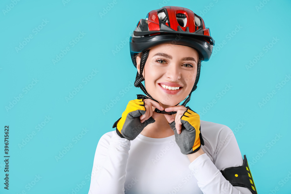 Female cyclist putting on helmet against color background