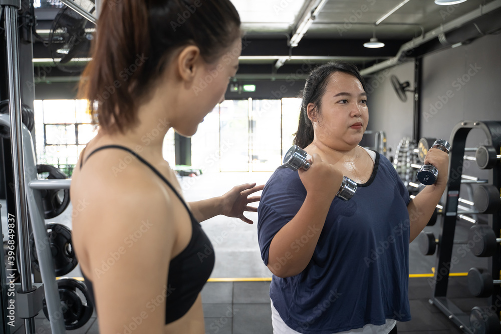 plump chubby Asian woman with personal trainer help gain muscle and lose fat in gym with fitness exe