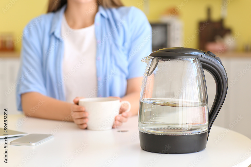 Electric kettle and woman with cup in kitchen, closeup