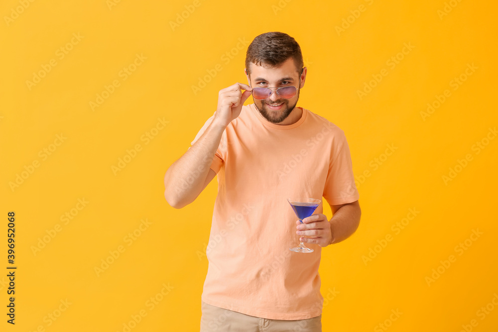 Handsome man with stylish sunglasses and cocktail on color background