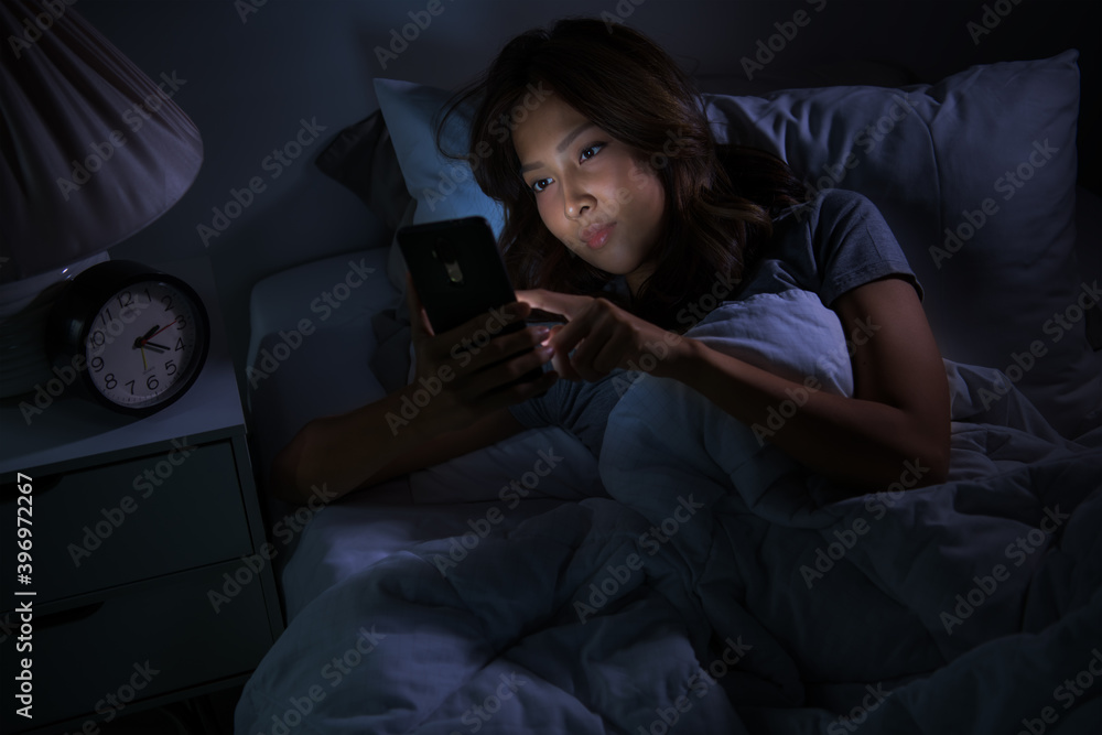 Young woman using a smartphone in her bed at night