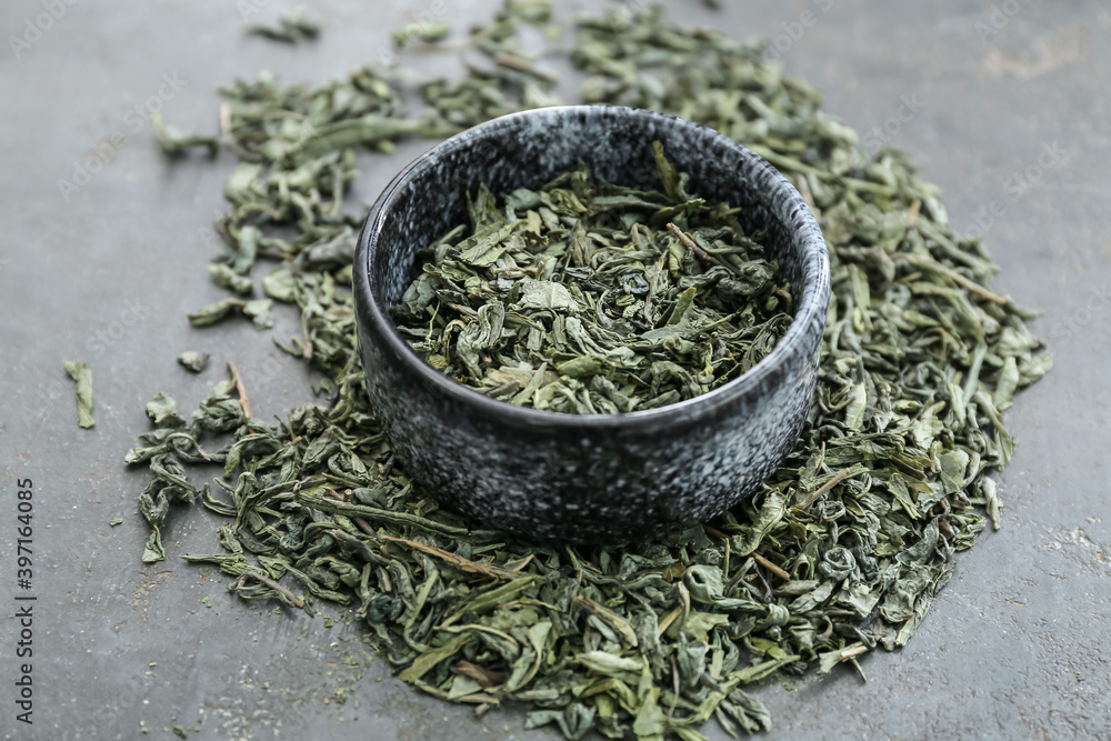 Bowl with dry green tea on dark background