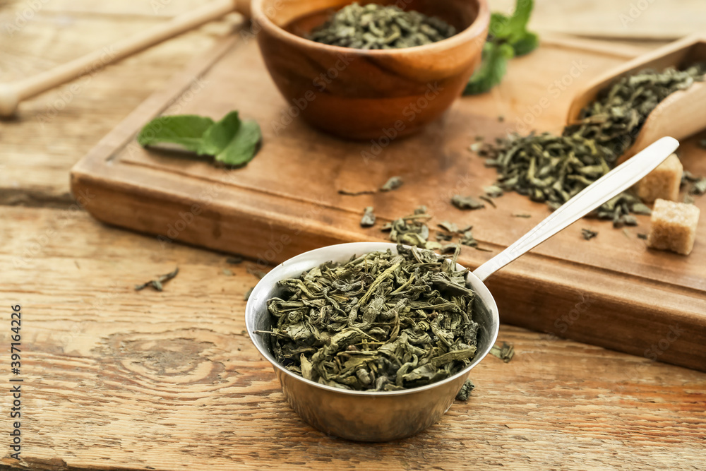 Scoop with dry green tea on wooden table