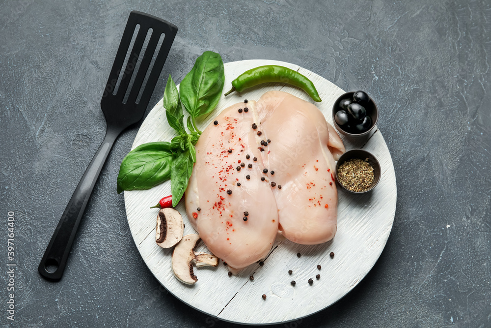 Board with raw chicken fillet on dark background