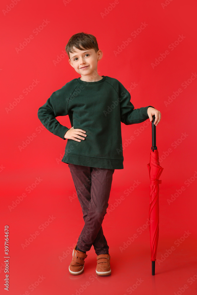 Cute little boy in autumn clothes and with umbrella on color background